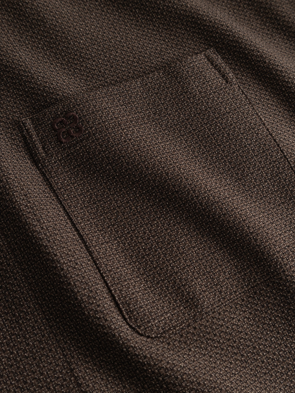 Close-up of the Gabba GABjens Over Rubin LS Overshirt in Brown Slate, showcasing its textured brown stretch dobby fabric with a pocket and an embroidered logo on the upper left corner of the pocket. The fabric features a subtle, repeating pattern commonly found in oversized fit overshirts.