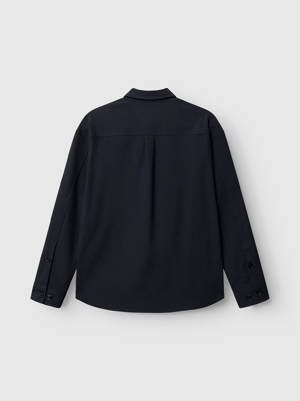The GABjens Over Rubin LS Overshirt by Gabba in blue black is displayed from the back against a plain light grey background. This oversized, long-sleeve button-up shirt features a collar, buttoned cuffs, and a straight hem.