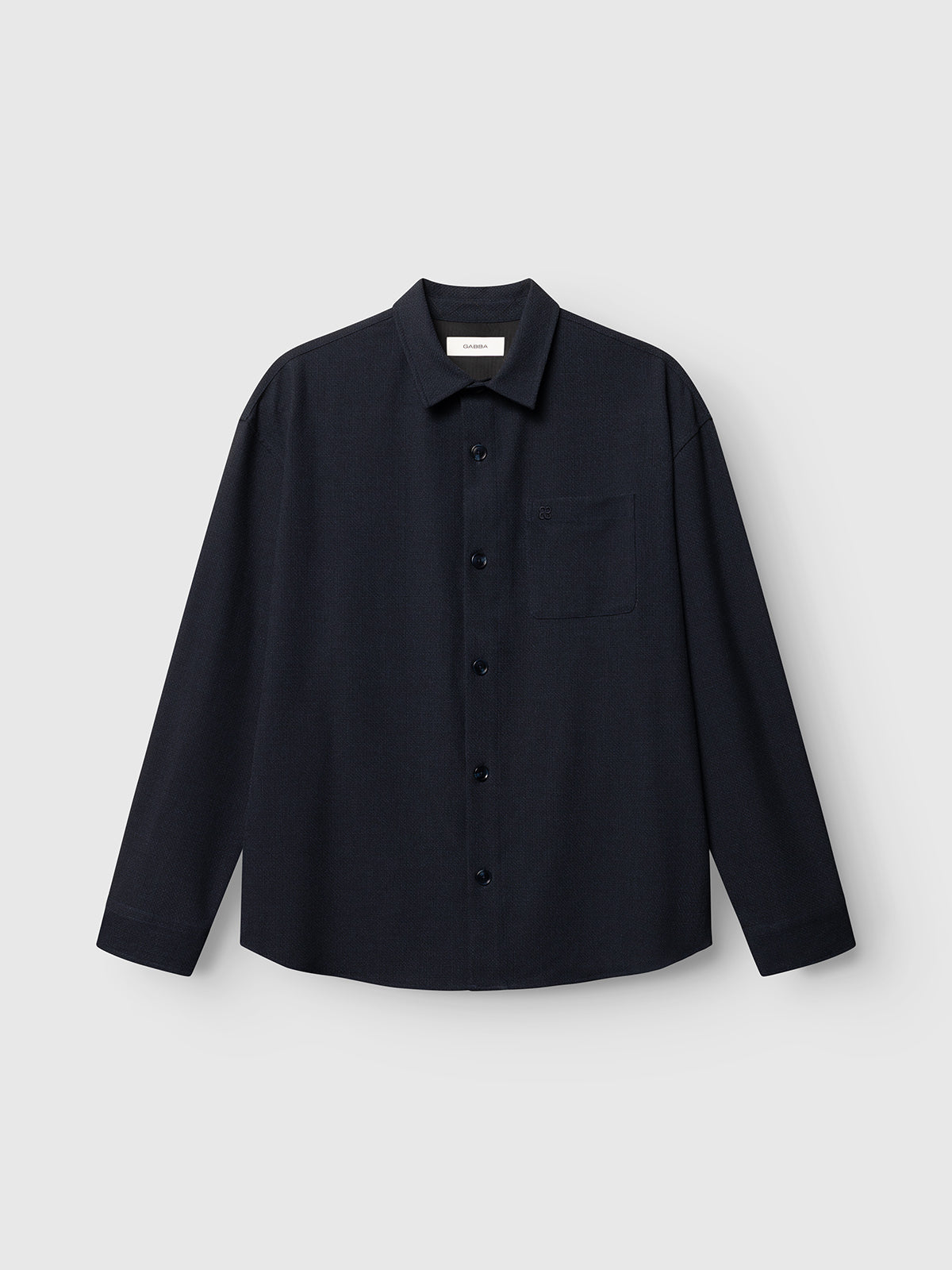 The GABjens Over Rubin LS Overshirt by Gabba, featuring a blue black hue, an oversized fit, stretch dobby fabric, a single chest pocket, and long sleeves, is laid flat on a light gray background.