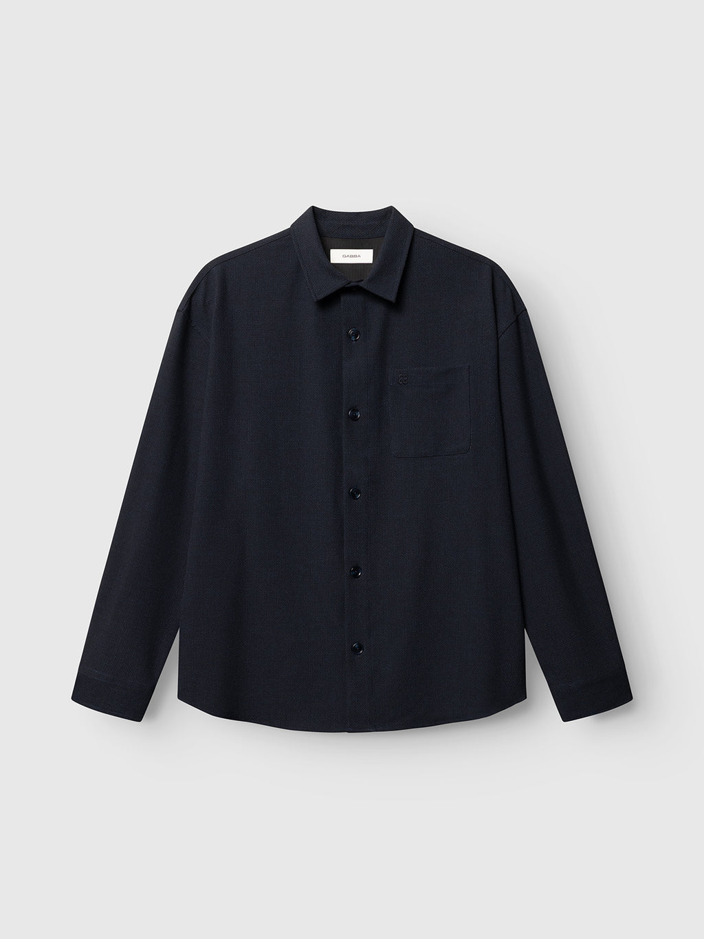 The GABjens Over Rubin LS Overshirt by Gabba, featuring a blue black hue, an oversized fit, stretch dobby fabric, a single chest pocket, and long sleeves, is laid flat on a light gray background.