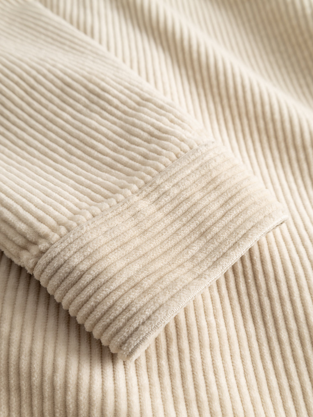 A close-up of the Gabba GABbeta Ibre LS Overshirt in Birch, showcasing the soft, ribbed texture and vertical ridges of its beige stretch corduroy sleeve as it rests on matching fabric—a versatile layering essential for everyday style.