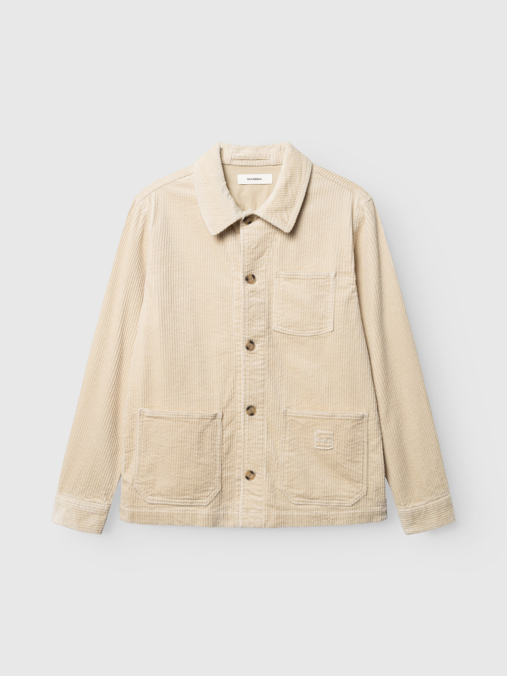 The GABbeta Ibre LS Overshirt in Birch by Gabba features a beige stretch corduroy construction with a collar, long sleeves, button-up front, and three utility pockets. Displayed on a plain light grey background, this versatile overshirt is a true layering essential for any wardrobe.