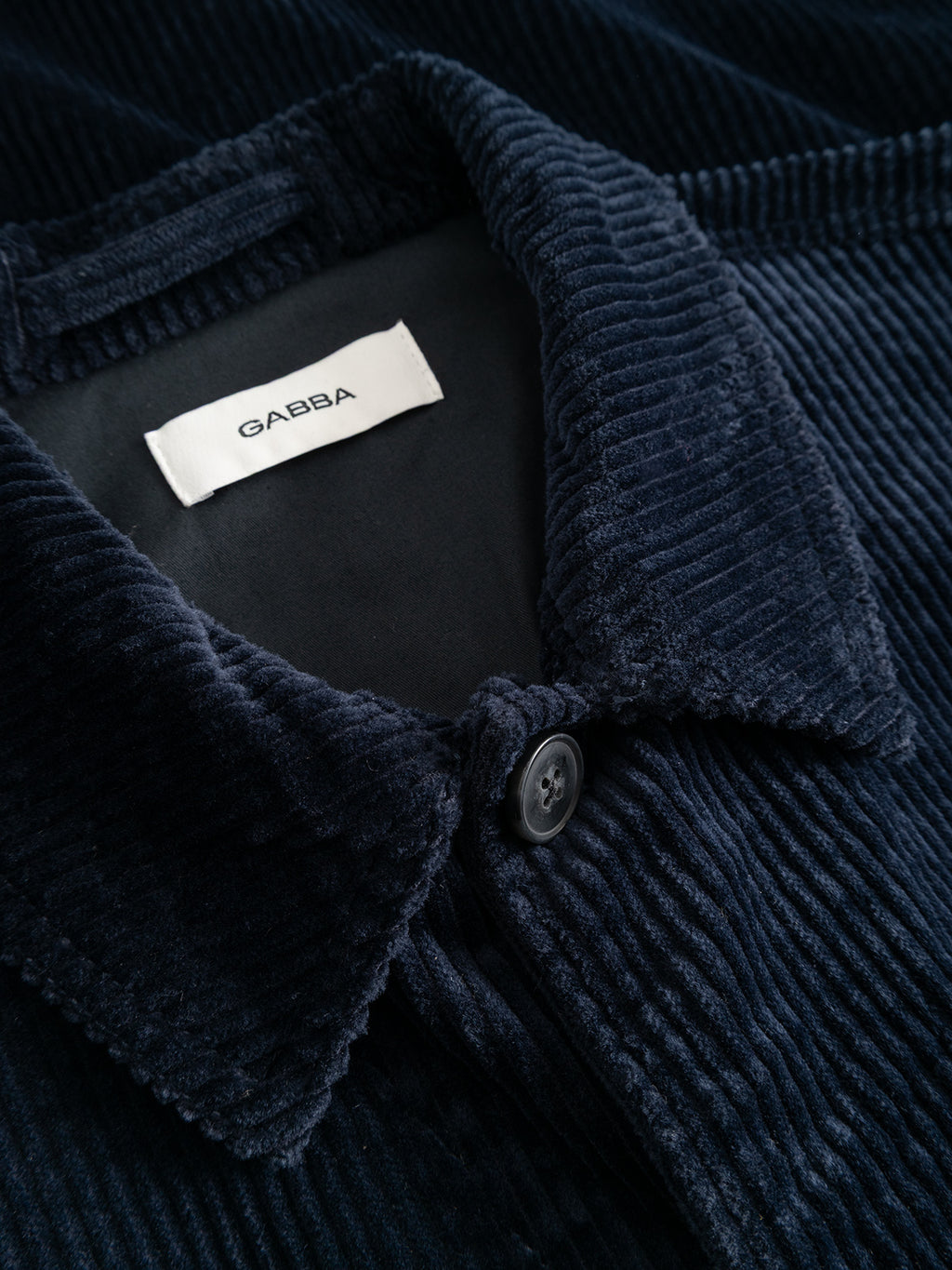 Close-up of the GABbeta Ibre LS Overshirt by Gabba in dark navy stretch corduroy, featuring a visible collar, button detail, and an inner white label with the Gabba name. This regular fit piece blends timeless style with modern comfort.