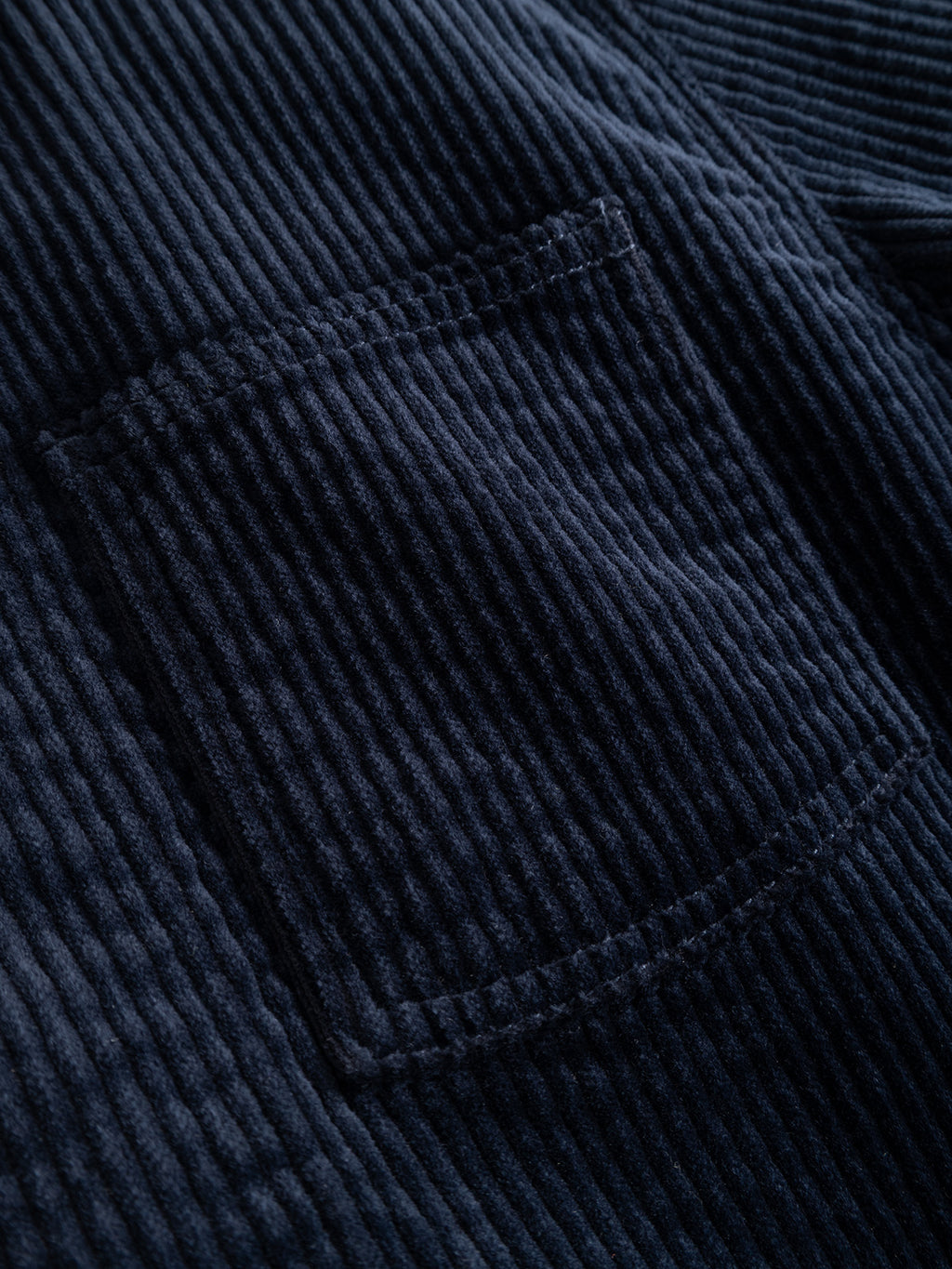 Close-up of the GABbeta Ibre LS Overshirt by Gabba in Dark Navy, featuring stretch corduroy fabric with visible parallel ridges and a soft, velvety texture. A rectangular utility pocket with prominent stitching is showcased on the garment.