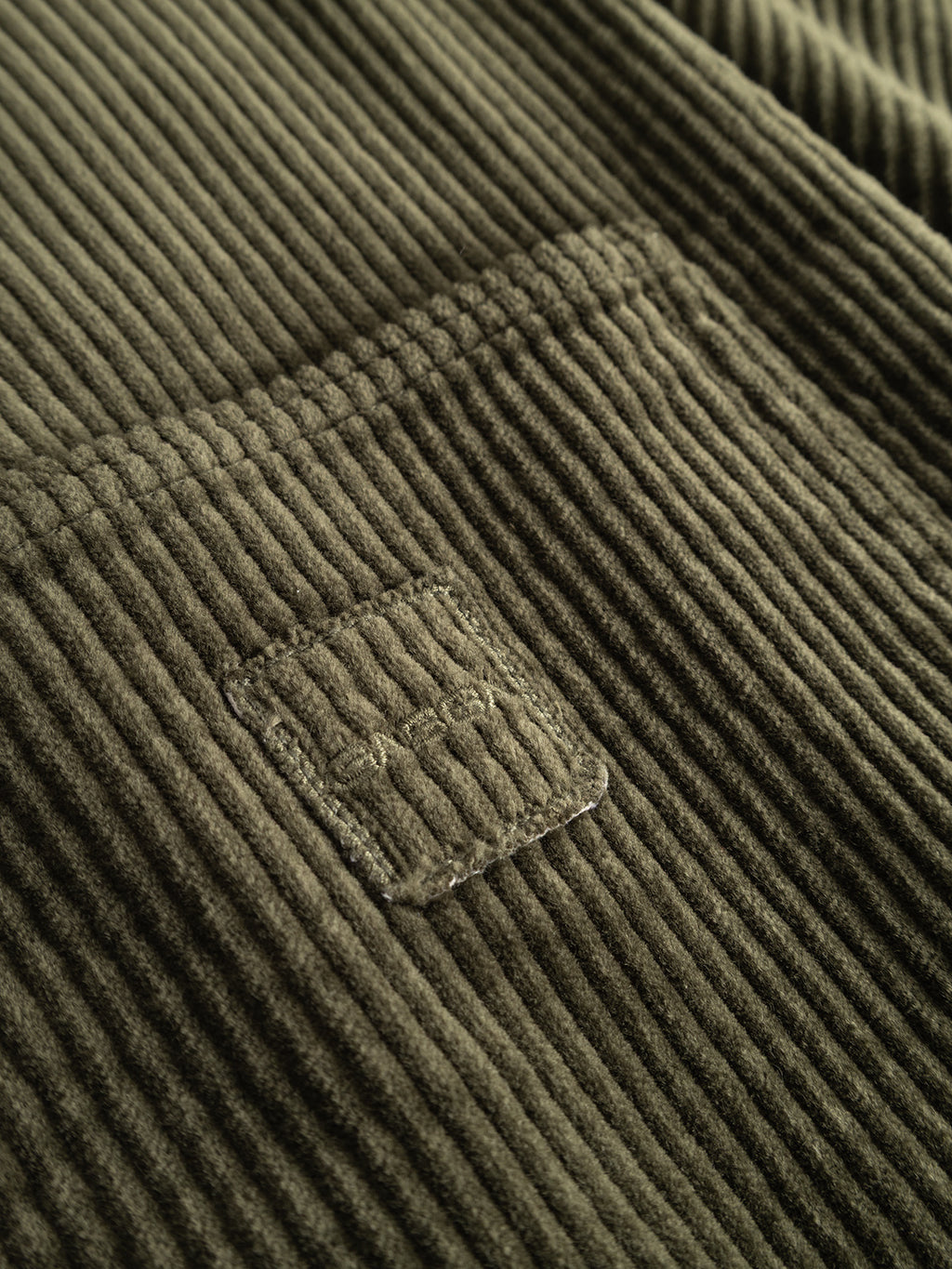 Close-up of the Gabba GABbeta Ibre LS Overshirt in Forest Night, featuring olive green stretch corduroy fabric with a visible pocket, detailed stitching, and a small rectangular patch. The pronounced texture and ridges of the material showcase its appeal as a versatile layering essential.