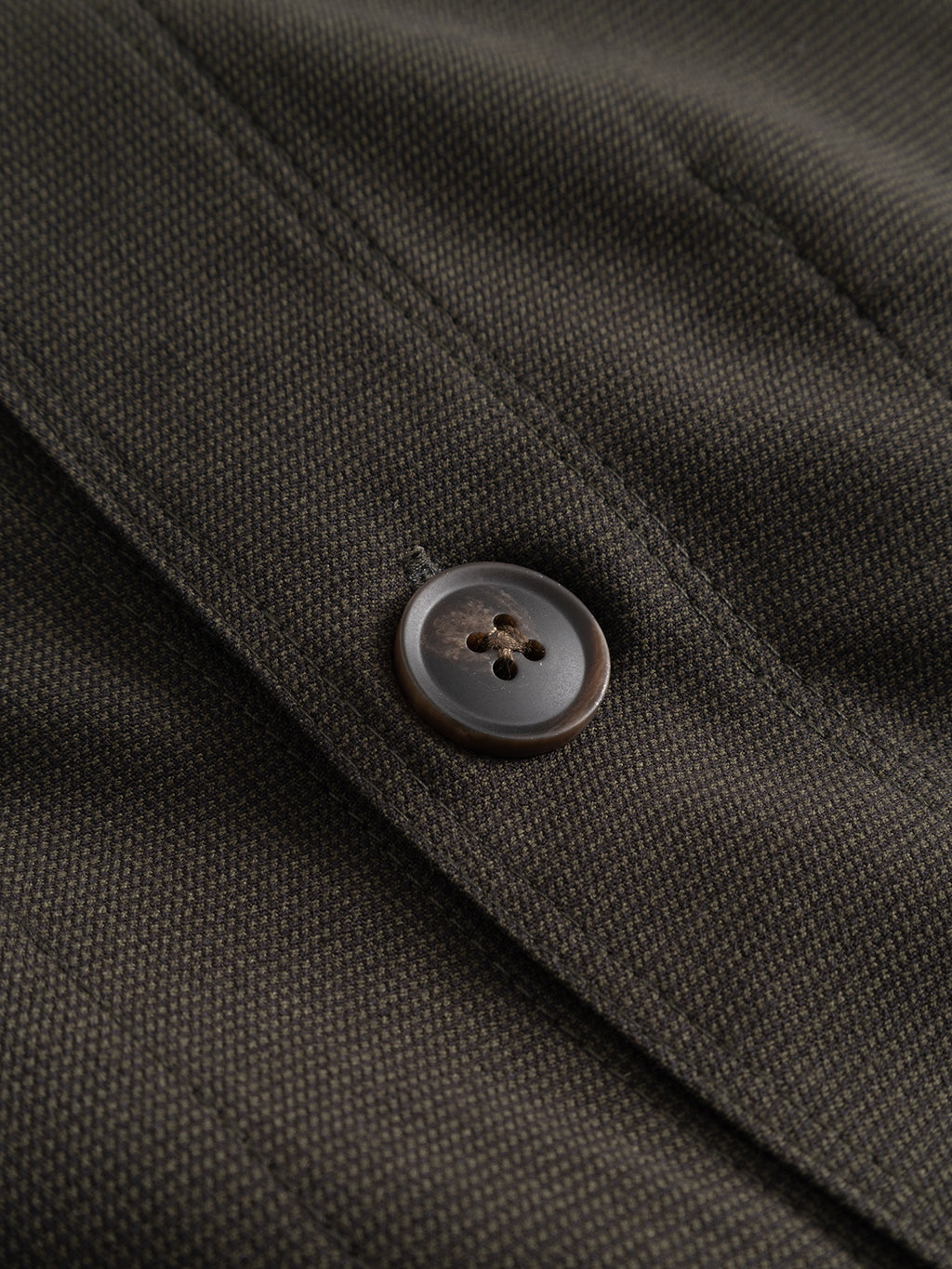 Close-up of the Gabba GABtogger Base Deme LS Overshirt in Forest Night, featuring a dark brown or charcoal micro-pattern woven fabric with a black and brown round four-hole button sewn onto it.