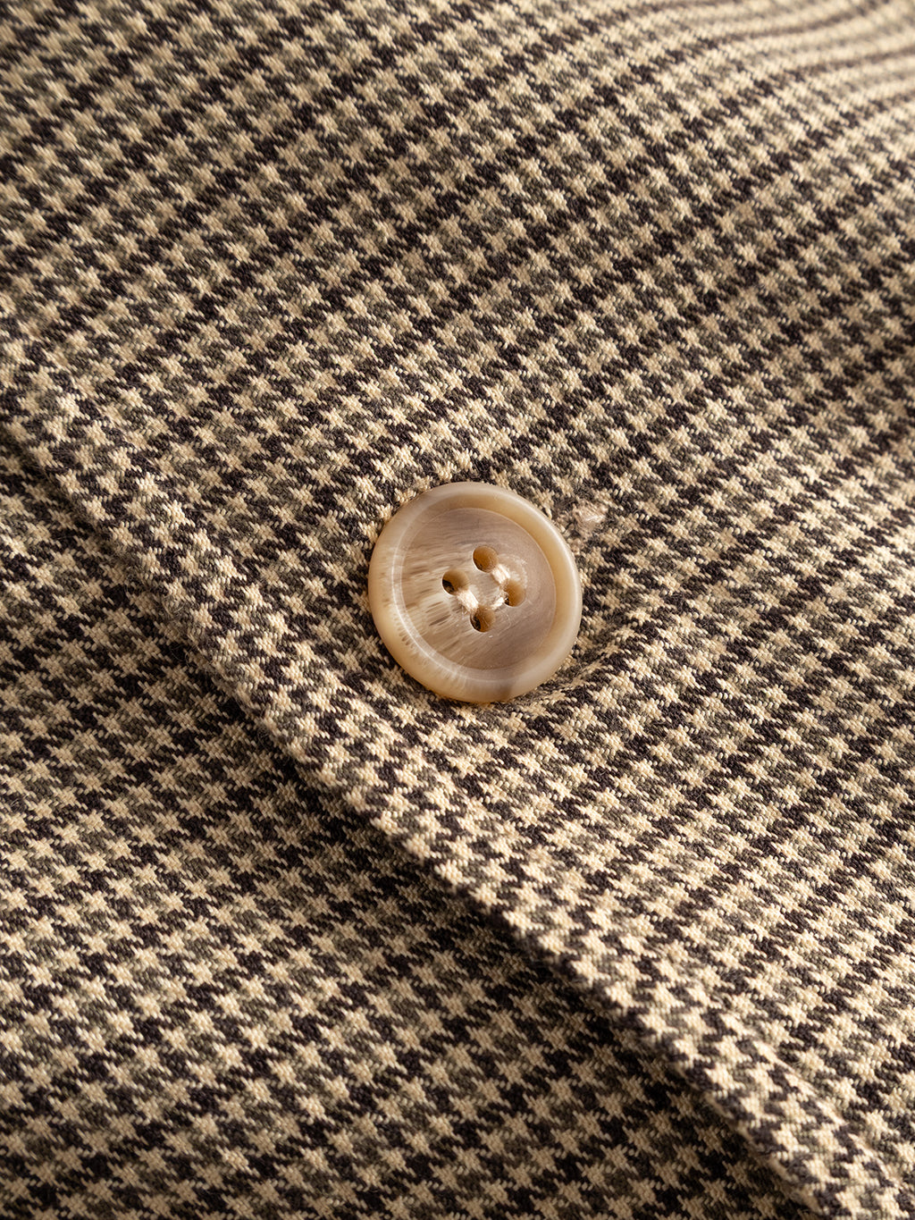 Close-up of the Gabba GABfelix Brit LS Shirt in Dark Sand, featuring a brown and beige houndstooth patterned lightweight woven fabric with a beige, round, four-hole button sewn on it.