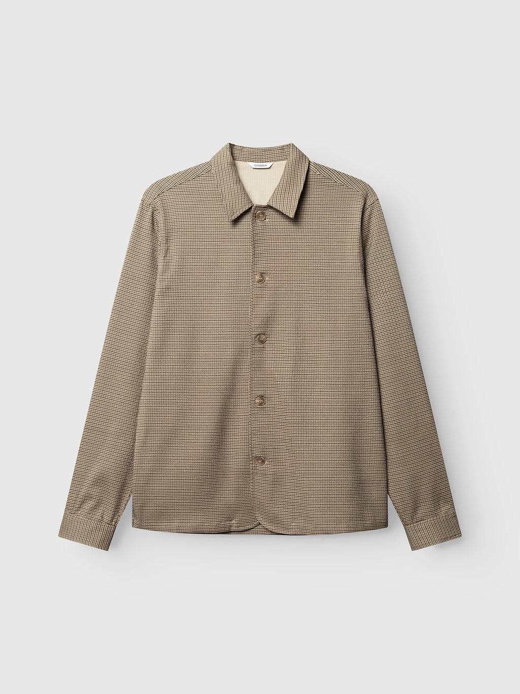 The Gabba GABfelix Brit LS Shirt in Dark Sand is a relaxed fit style featuring long sleeves and a button-up front, crafted from lightweight woven fabric with a subtle micro-check pattern in brown. Designed with a standard collar and brown buttons, this shirt is displayed laid flat on a plain white background.