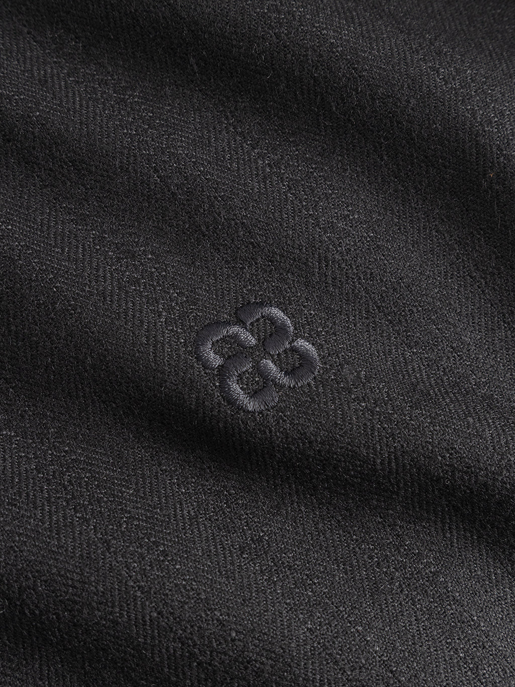 Close-up of the Gabba GABfelix Fuyu LS Shirt in Meteorite, featuring a black viscose-blend fabric with a subtle herringbone pattern and an embroidered geometric logo at the center—perfect for everyday wear.