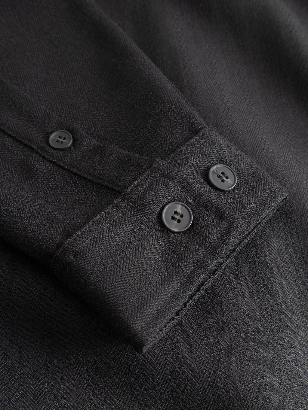 Close-up of the GABfelix Fuyu LS Shirt - Meteorite by Gabba, showcasing a black shirt cuff with two black buttons. The comfortable viscose-blend fabric features a subtle herringbone pattern, ideal for everyday wear, and part of the sleeve with an additional button is also visible.
