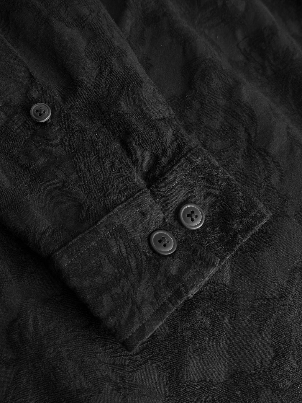 Close-up of the GABjens Over Brocade LS Shirt by Gabba in black, showcasing the cotton-blend cuff with a subtle jacquard floral pattern, two black buttons, and visible stitching details.