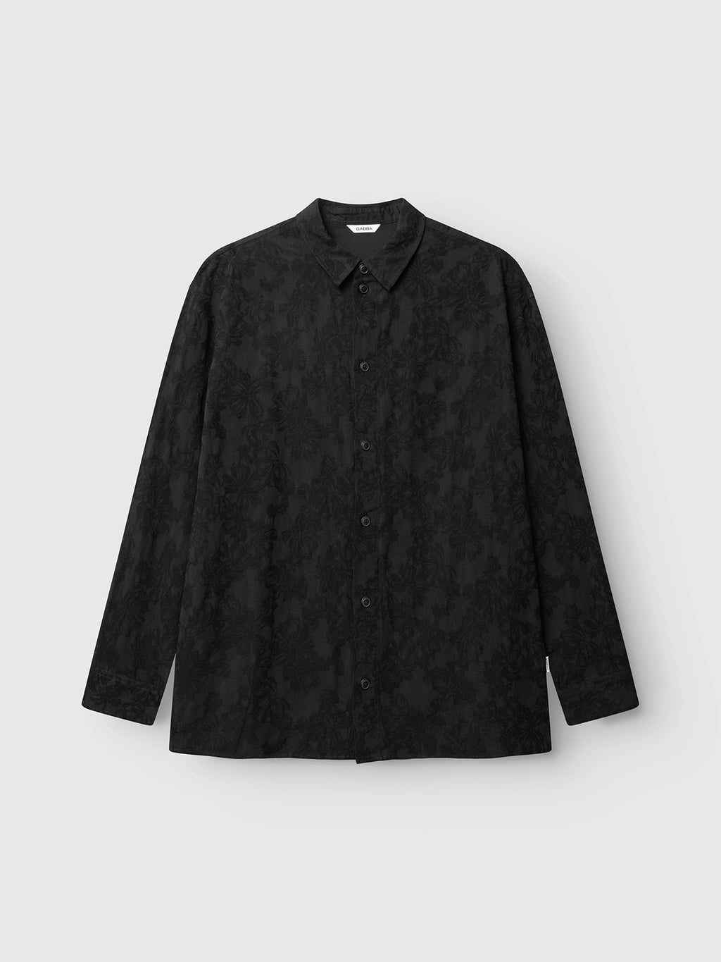 Gabba GABjens Over Brocade LS Shirt in black, an oversized long-sleeve button-up featuring a subtle jacquard floral pattern and crafted from a soft cotton-blend, shown laid flat on a light gray background.