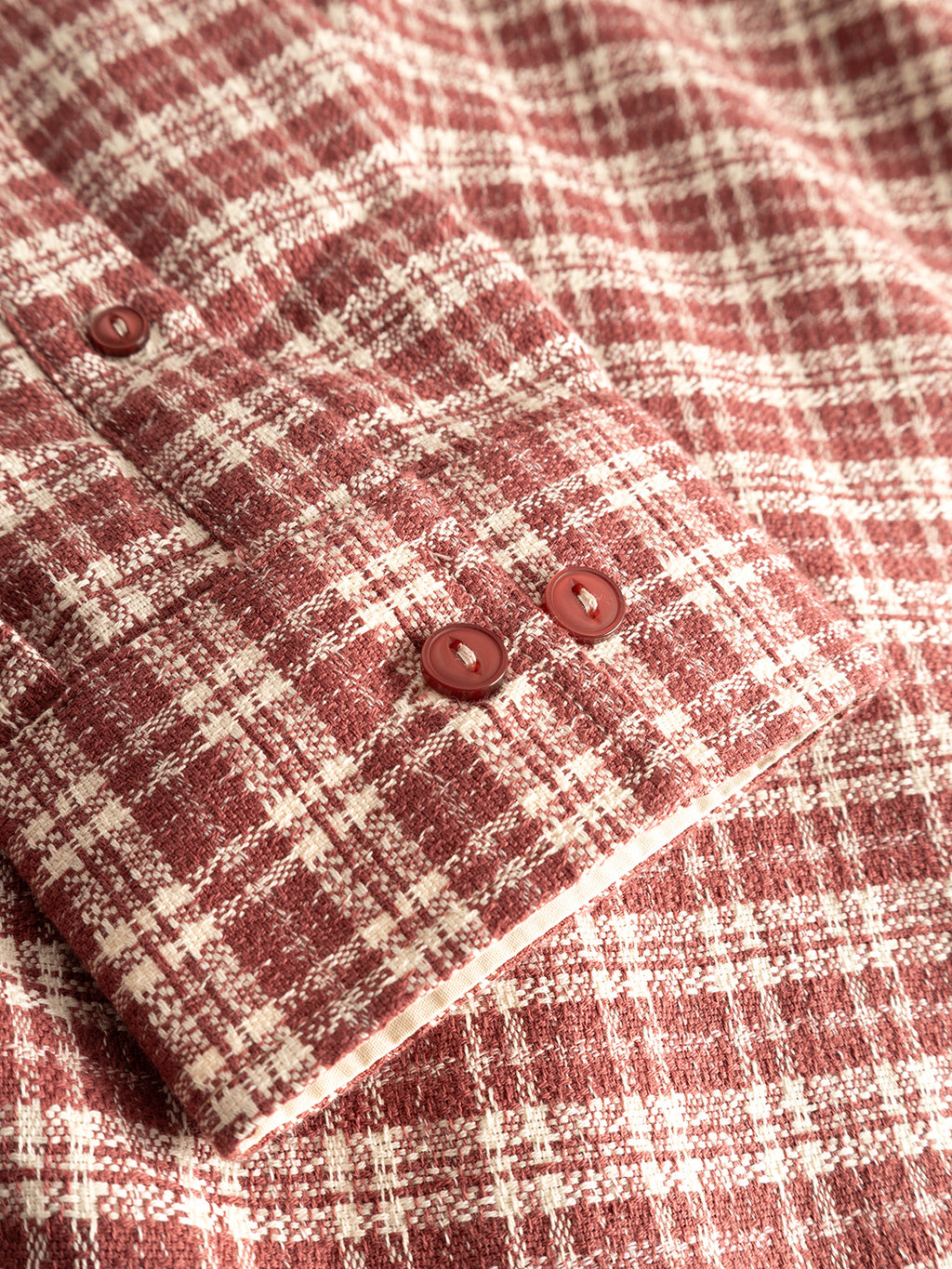 Close-up of the GABsven Reg TX2 LS Shirt in Brick Red by Gabba, showcasing the cuff with two red buttons. Crafted from yarn-dyed cotton, the fabric displays a soft, textured finish with a red and white checkered pattern formed by intersecting lines and squares.