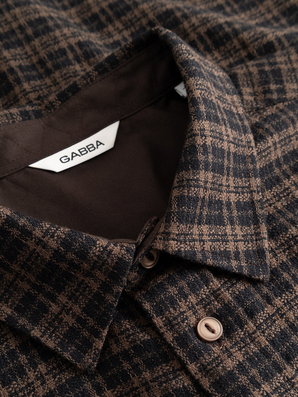 Close-up of the GABsven Reg TX2 LS Shirt in Brown Slate by Gabba, showing its brown and black checked texture with buttons. The shirt label inside the collar displays the Gabba brand name.