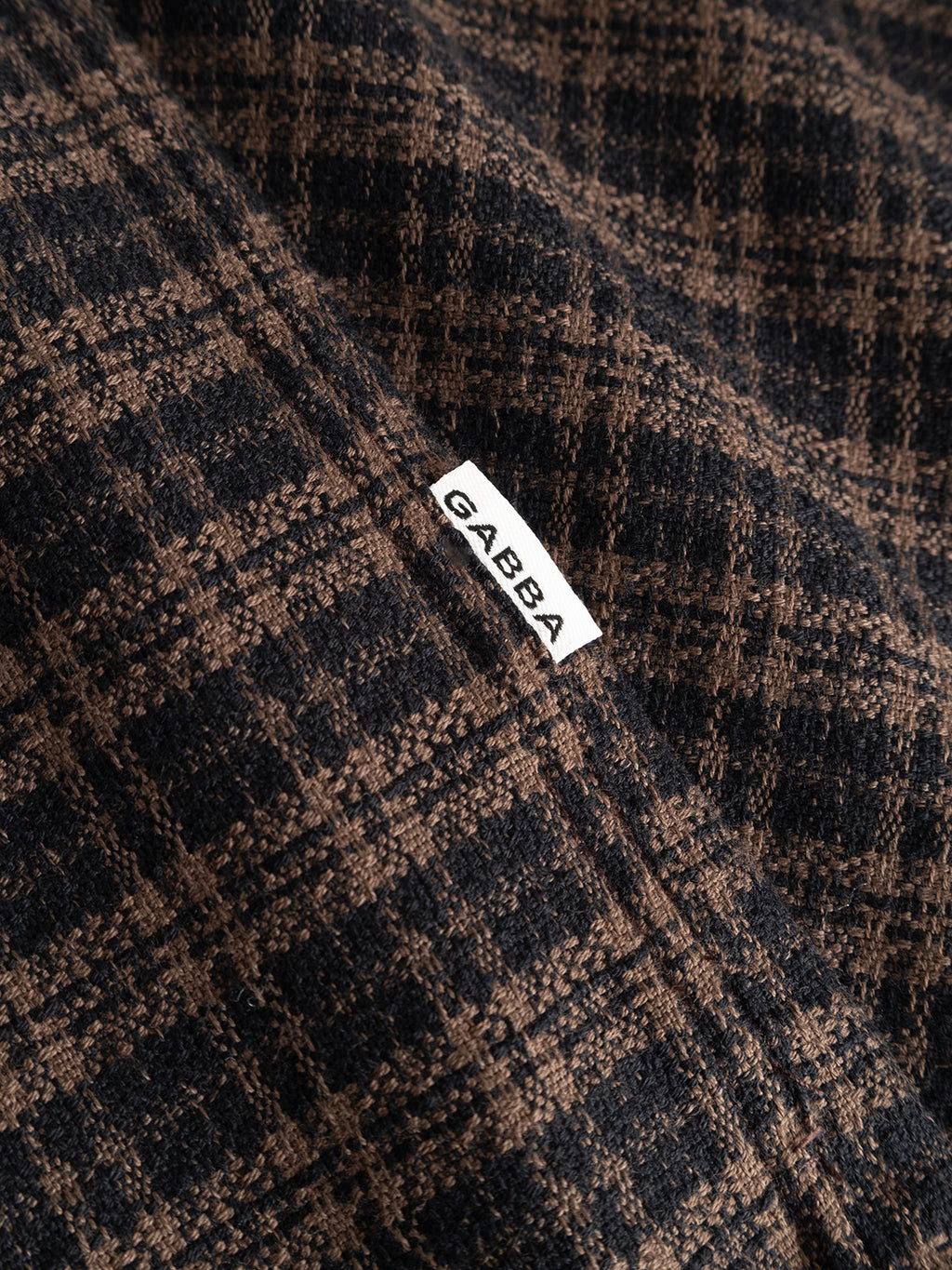 Here’s a rewritten version using your product data: Close-up of the GABsven Reg TX2 LS Shirt in Brown Slate by Gabba, featuring a brown and black checkered pattern and a small white label with the Gabba logo, showcasing the premium yarn-dyed cotton texture and regular fit.