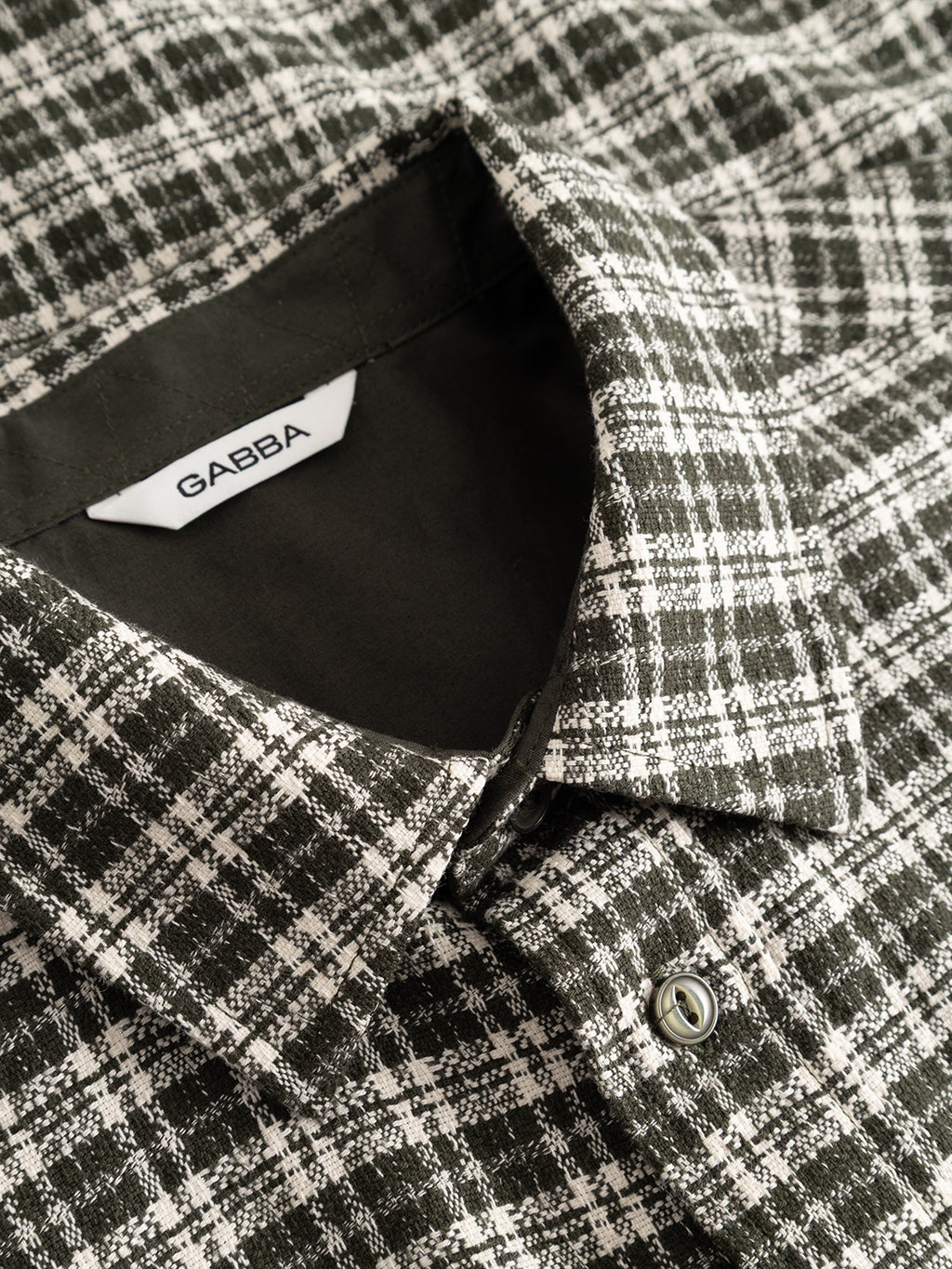 Close-up of the GABsven Reg TX2 LS Shirt - Forest Night by Gabba, a yarn-dyed cotton black and white plaid shirt featuring a pointed collar, button detail, and an inner collar tag with “Gabba” in black lettering. This regular fit shirt showcases a classic checked texture for timeless appeal.