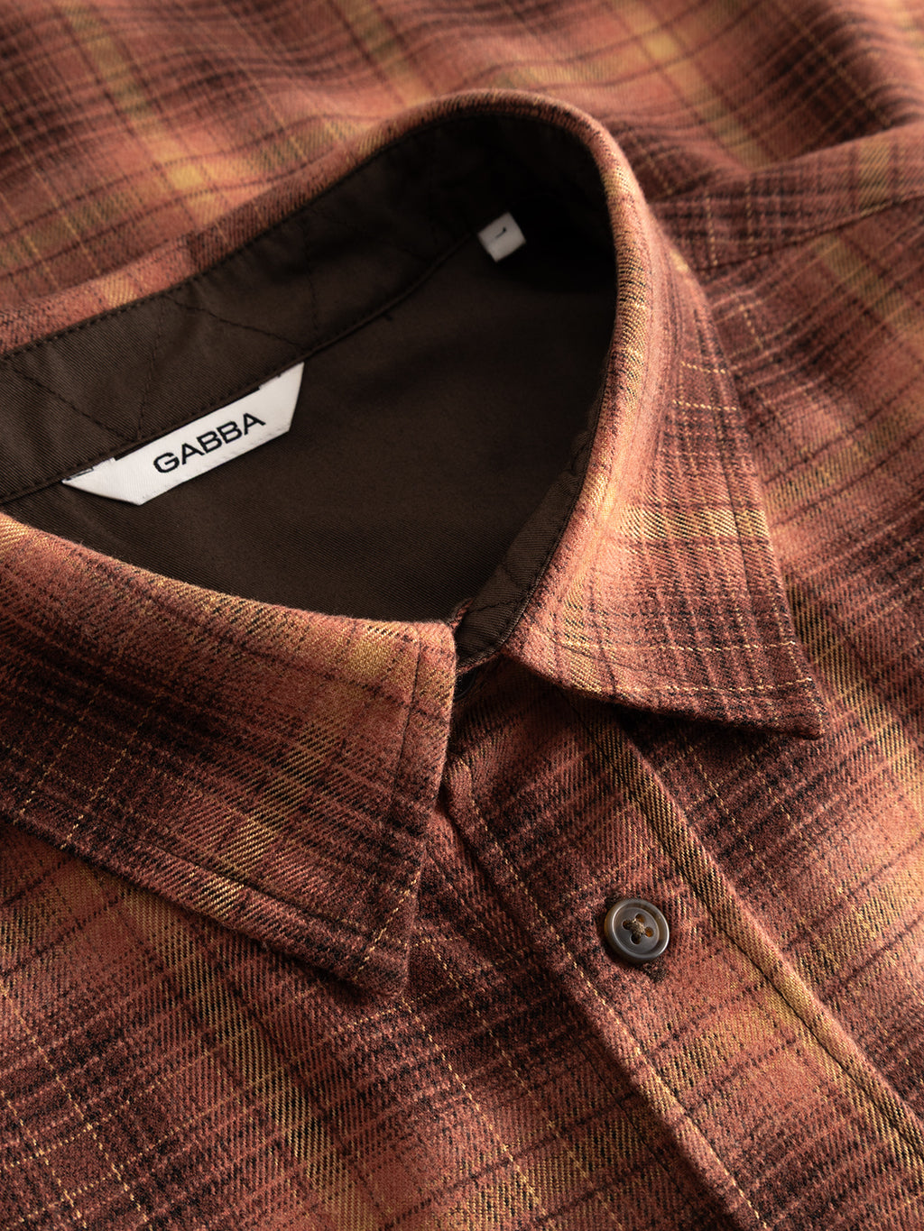 Here is your rewritten sentence using the provided product data: Close-up of a Gabba GABsven Reg F1097 LS Shirt in brick red, featuring a regular fit and crafted from a stretch-viscose blend. The checked texture accentuates the collar, button placket, and Gabba brand label against a contrasting dark lining.