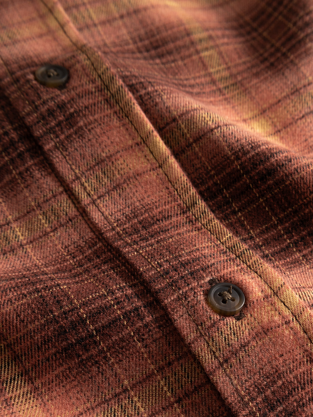 A close-up view of the Gabba GABsven Reg F1097 LS Shirt in Brick Red highlights its distinctive plaid pattern in shades of brown, yellow, and black, with a regular fit and two dark buttons along the front.