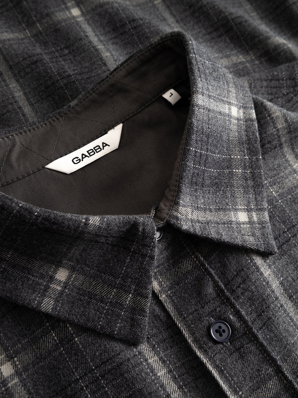 Close-up of the GABsven Reg F1097 LS Shirt - Night Sky by Gabba, showcasing its gray plaid pattern with black buttons and a white brand label inside the collar. The fabric has a checked texture and a soft, textured appearance.