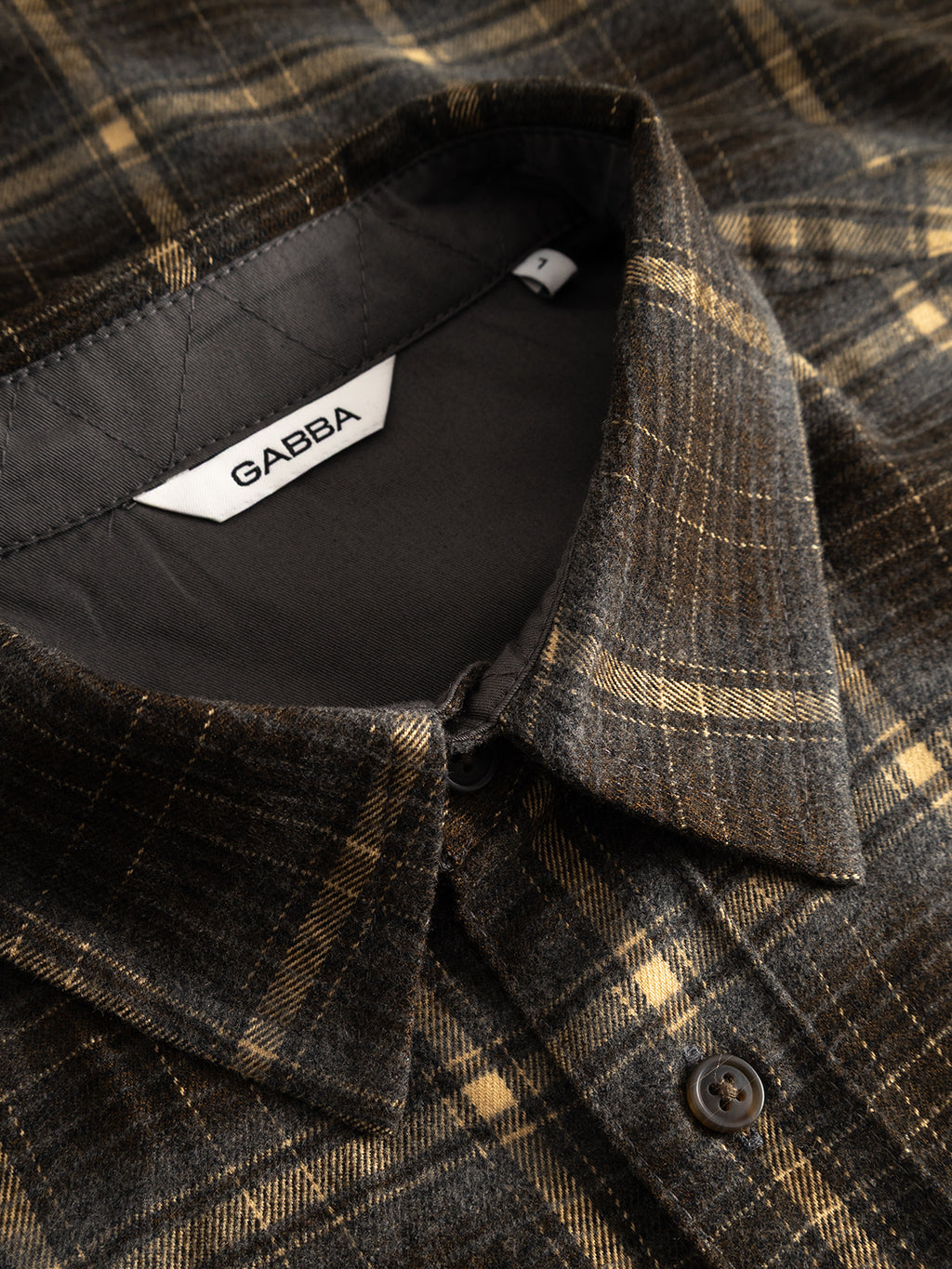 Close-up of the GABsven Reg F1097 LS Shirt by Gabba in Forest Night—a brown and yellow plaid shirt with a collar and buttons, showcasing a checked texture. The inside label displays “Gabba” on a white tag. This regular fit shirt is crafted from a soft, textured stretch-viscose blend for enhanced comfort.