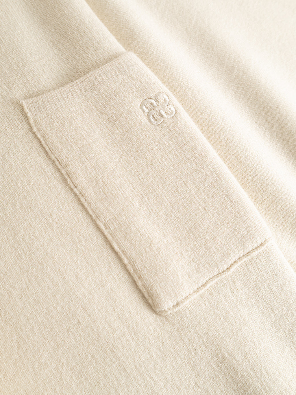 Close-up of the GABadriel Zip Lume LS Knit - Birch by Gabba, featuring a beige viscose blend knit fabric pocket with subtle embroidered “CB” initials above the pocket opening; the texture appears soft and smooth.