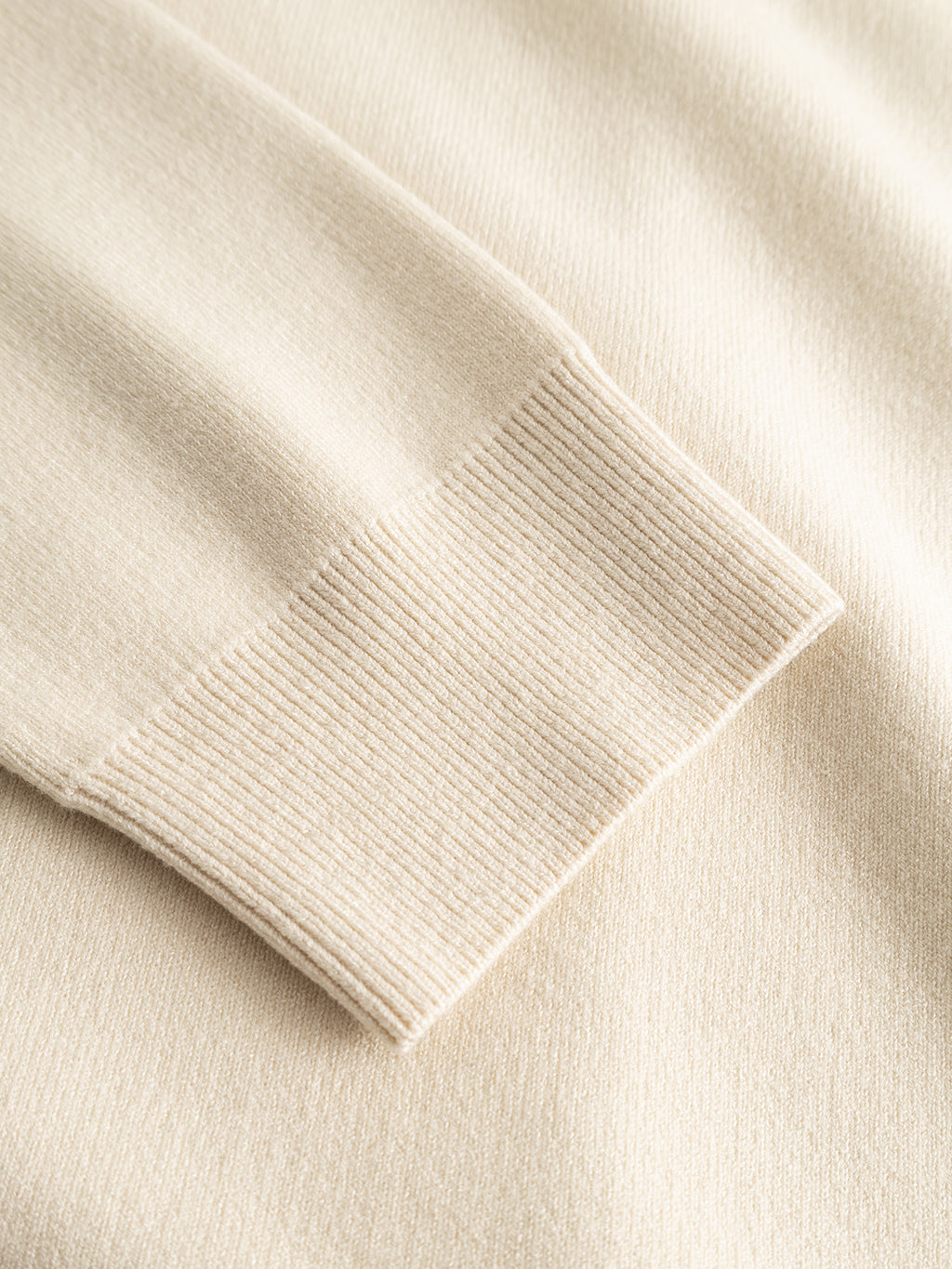 Close-up of the GABadriel Zip Lume LS Knit - Birch by Gabba, featuring a regular fit sleeve crafted from a viscose blend knit with a ribbed cuff, laid flat on a matching fabric background.