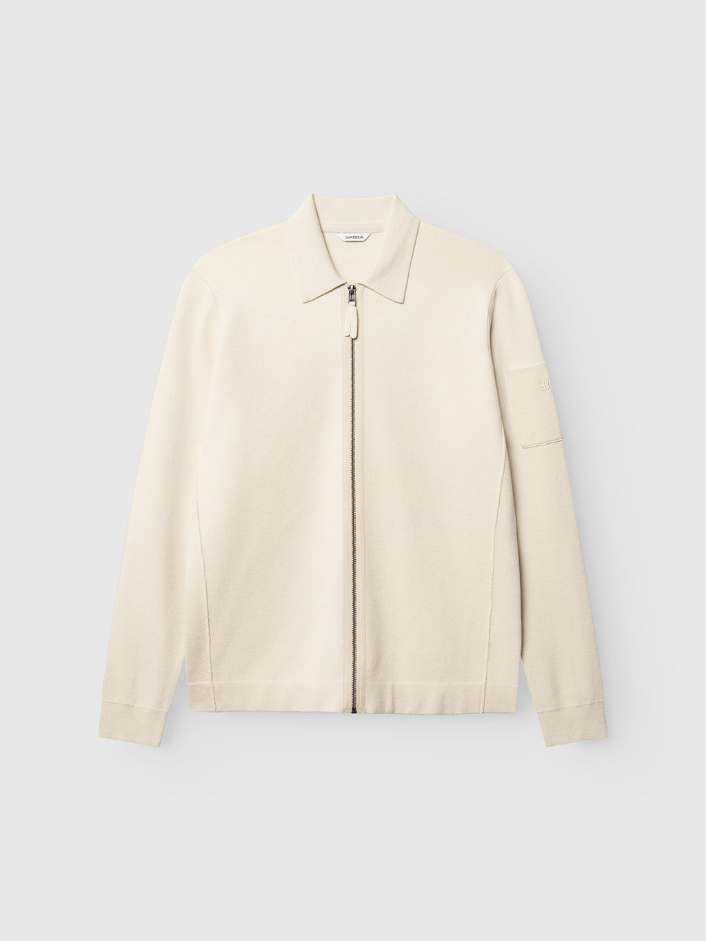 The GABadriel Zip Lume LS Knit - Birch by Gabba is a cream-colored viscose blend zip-up jacket with a collar and long sleeves, shown against a plain light gray background. This minimalist jacket features a subtle sleeve pocket and a full zip closure.