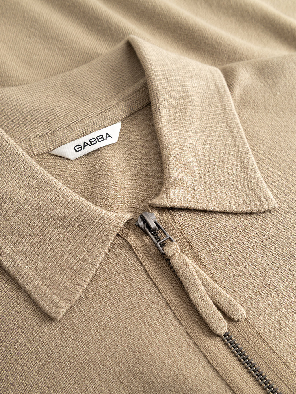 Close-up of the GABadriel Half Zip Lume LS Knit in Sand Crocker by Gabba, a beige long-sleeve knit crafted from a soft viscose blend, featuring a half-zip and an inner collar label.