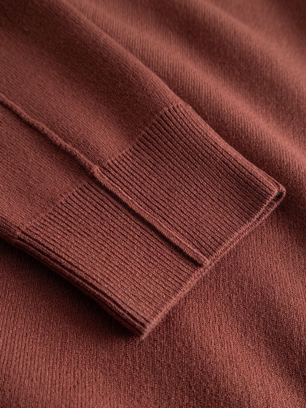 Close-up of the GABadriel O-Neck Lume LS Knit sweater by Gabba in brick red, featuring a regular fit with detailed ribbed cuff texture and visible stitches.