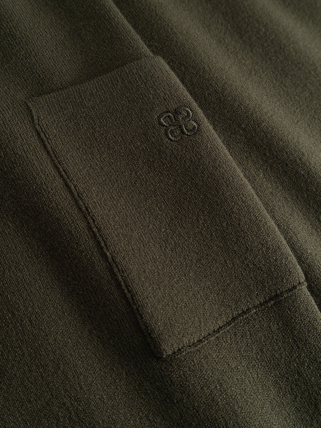 Close-up of the Gabba GABadriel O-Neck Lume LS Knit in Forest Night, showcasing its olive green, mid-weight viscose blend fabric. The regular-fit knit features a rectangular pocket with a small, subtle embroidered logo above it. The texture appears visibly soft and smooth.