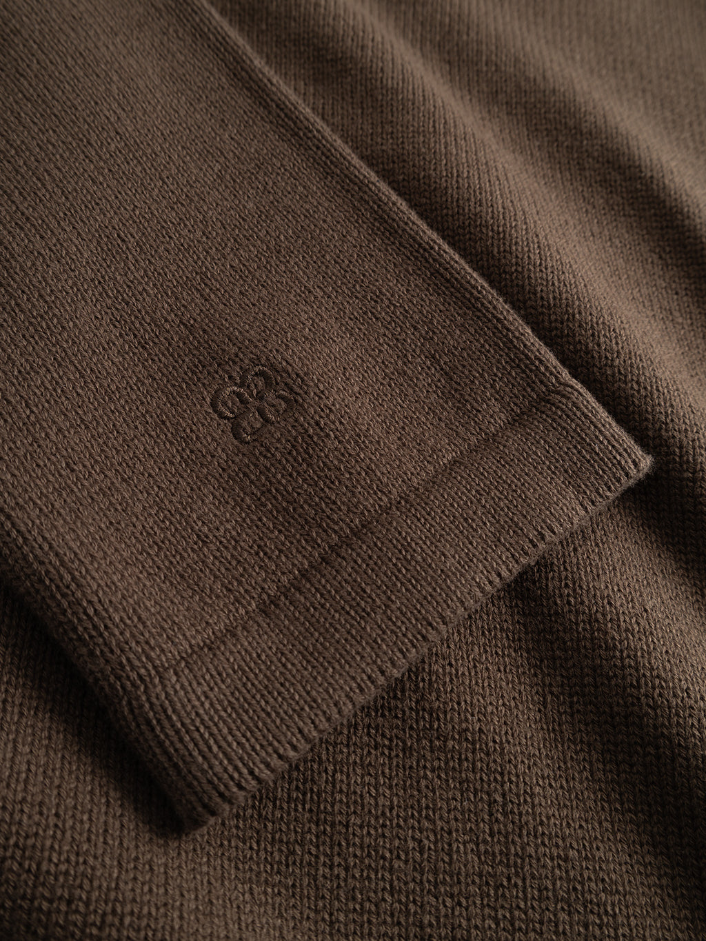 Close-up of a brown GABbenoit Cardi Fort LS Knit sleeve cuff featuring a small embroidered logo on the structured knit.