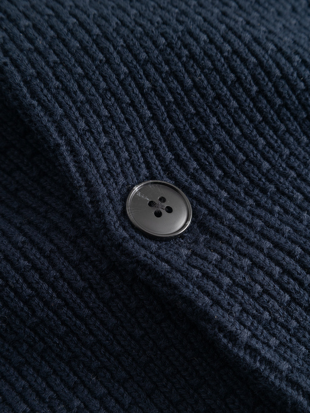 A close-up of a black button sewn onto the dark blue ribbed fabric of the Gabba GABbenoit Cardi Fort LS Knit - Night Sky cardigan.