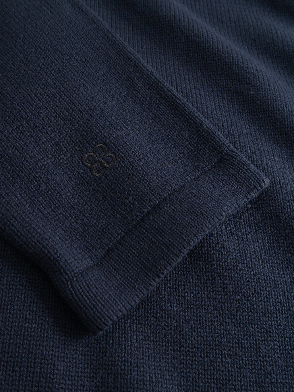 A close-up of the Gabba GABbenoit Cardi Fort LS Knit sweater in Night Sky, showing its structured knit sleeve with a subtle embroidered pattern near the cuff, lying flat on matching fabric.