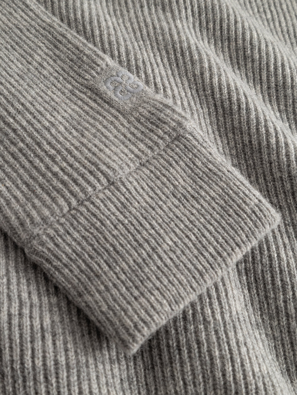 A close-up of the Gabba GABremy Cardi Flash LS Knit in Grey Mel highlights its relaxed fit, featuring a rib-knit sleeve with a small embroidered logo near the cuff.