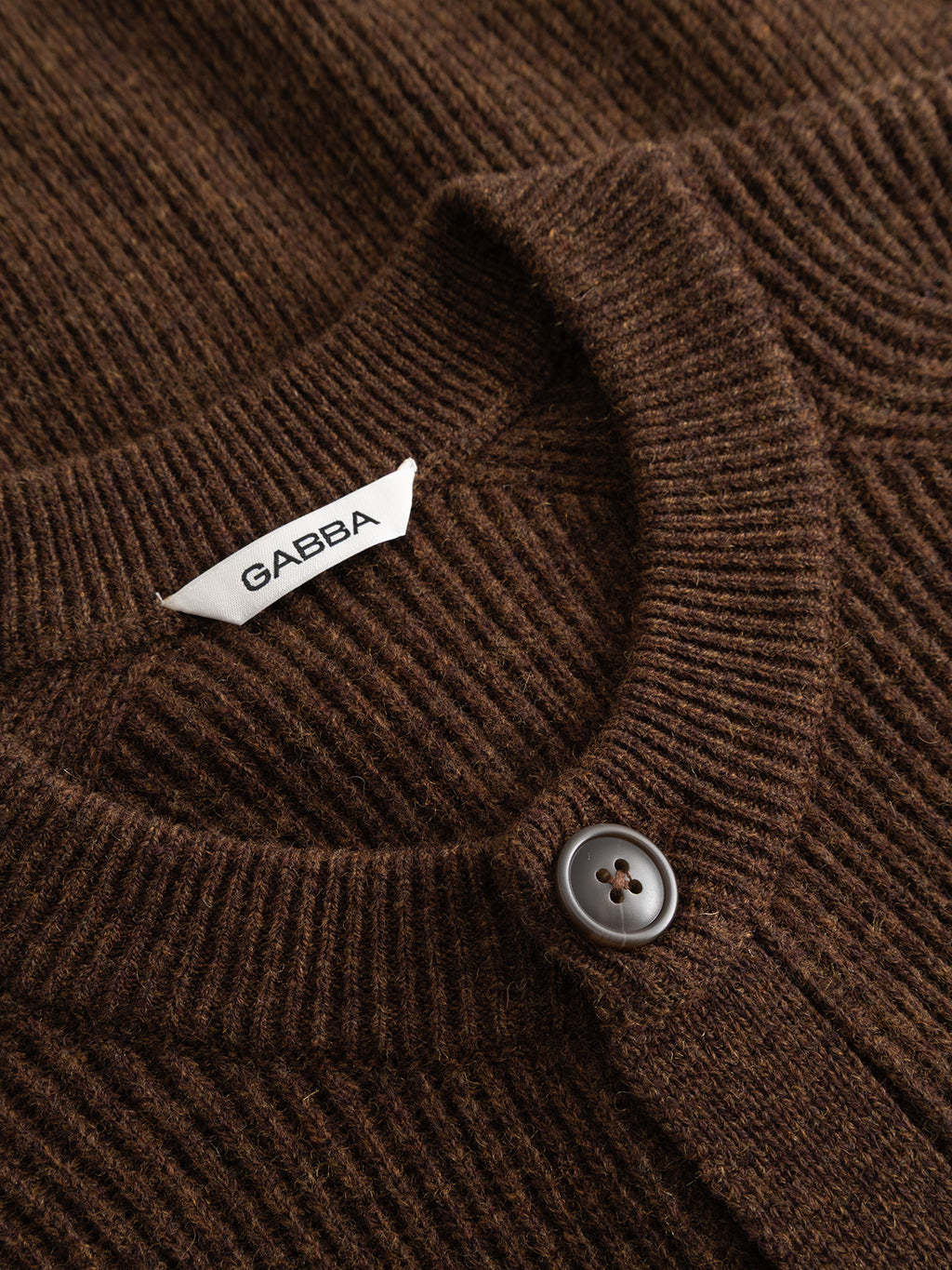 Close-up of the GABremy Cardi Flash LS Knit in Brown Slate by Gabba, a relaxed-fit rib-knit wool cardigan featuring a round collar, a dark gray button, and a white GABBA tag.