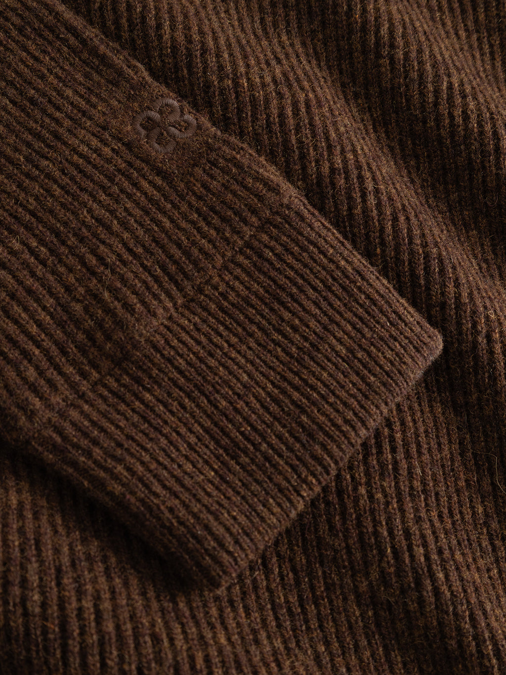 Close-up of the Gabba GABremy Cardi Flash LS Knit in Brown Slate, highlighting the sleeve’s tight vertical rib-knit pattern and a small embroidered clover or floral logo near the cuff.