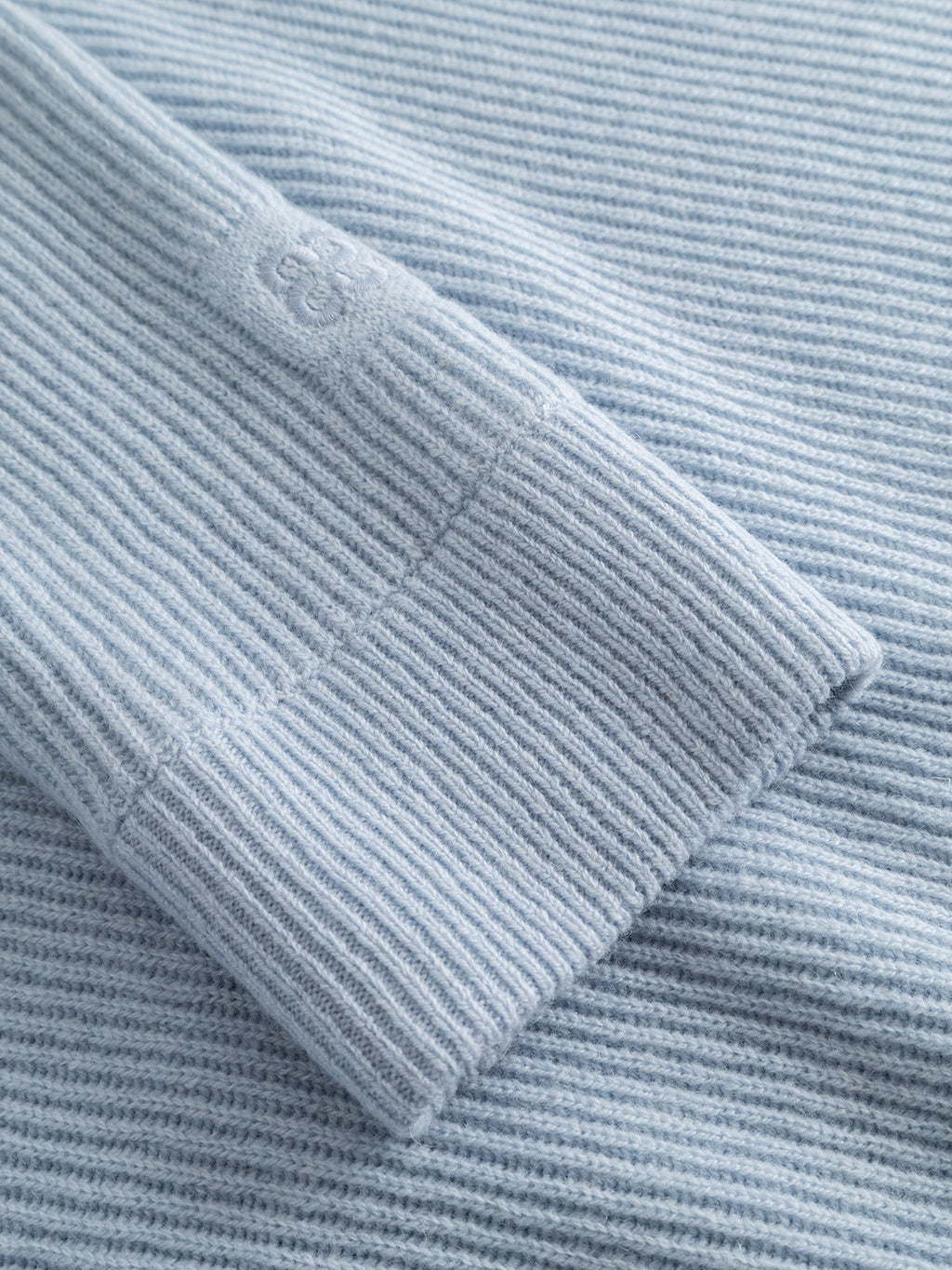 Close-up of the GABremy O-Neck Flash LS Knit by Gabba in Dusty Blue, showing the crew neck ribbed sweater sleeve resting on matching ribbed fabric and highlighting the relaxed-fit texture and knit pattern.