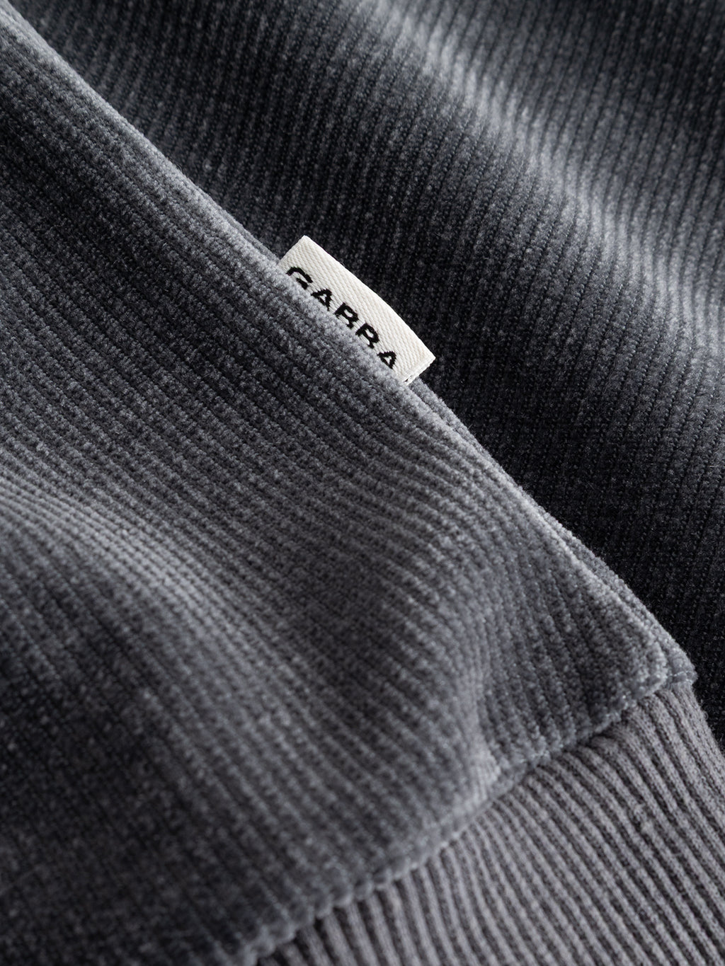 Close-up of blue ribbed jersey corduroy fabric from the Gabba GABprimo Fune Hoodie LS Sweat in Turbulence Blue, featuring a partially visible white label with lettering. The detailed texture and stitching highlight the relaxed vibe of this regular fit casual hoodie.