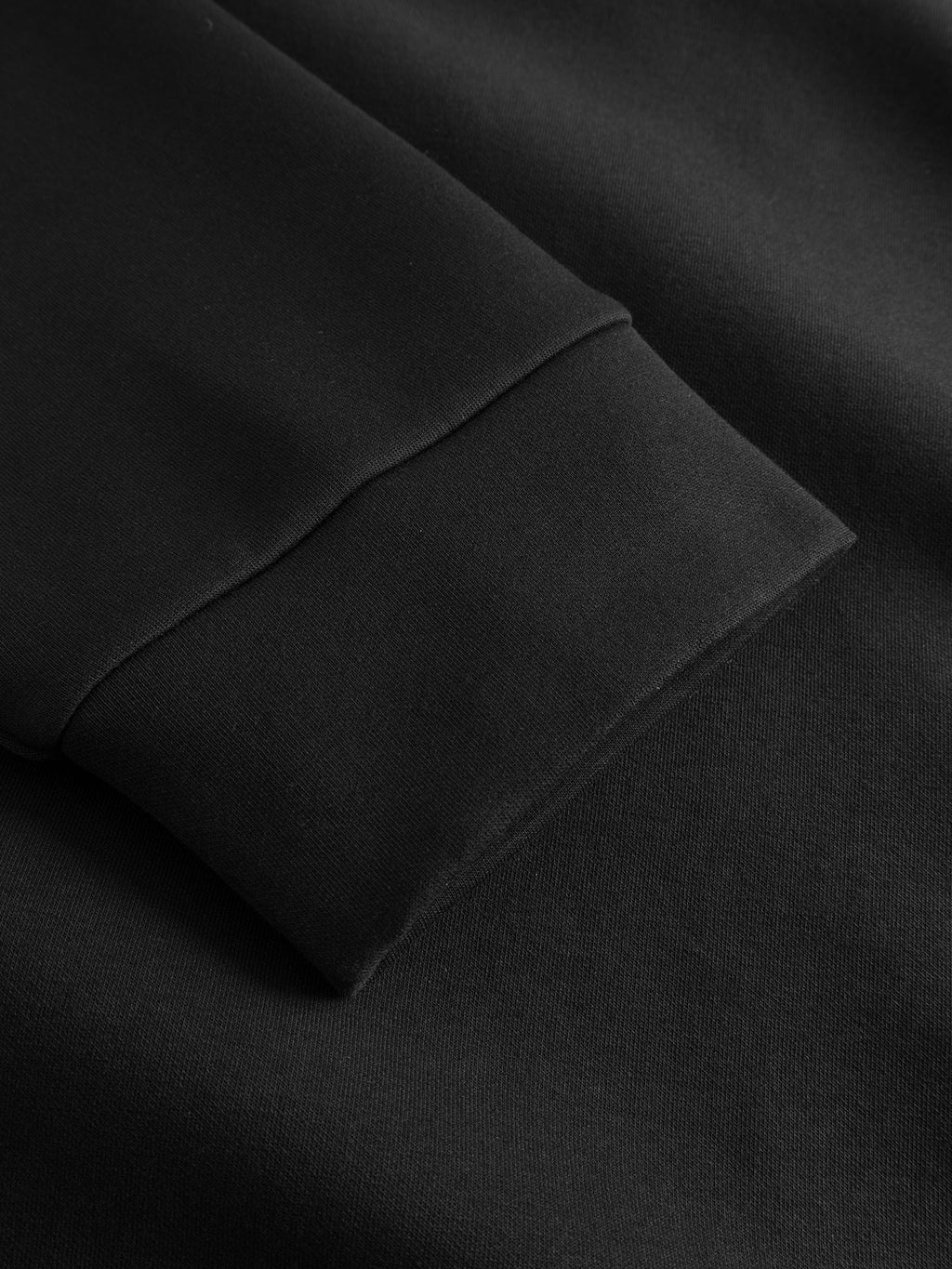 Close-up of the black long sleeve cuff on the Gabba GABnik Camp Lock Sweat - Meteorite, crafted from smooth, dark mid-weight interlock fabric—highlighting the texture and stitching details typical of this modern outerwear piece.