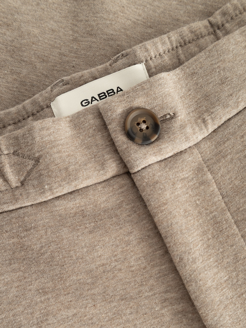 Close-up of the GABmonza Cropped Tasca Lock Pant in Sand Mel by Gabba, featuring a brown button and a visible white Gabba label; crafted from mid-weight interlock fabric in a relaxed straight fit.