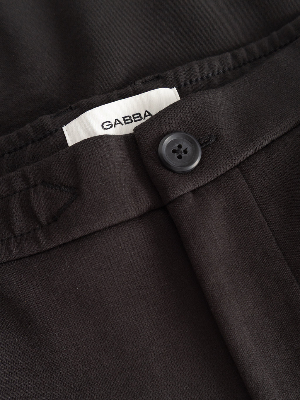 Close-up of the waistband of the Gabba GABmonza Cropped Tasca Lock Pant in Meteorite, featuring a black button and a white Gabba label. Crafted from mid-weight interlock fabric, these pants offer a relaxed straight fit designed for everyday comfort.