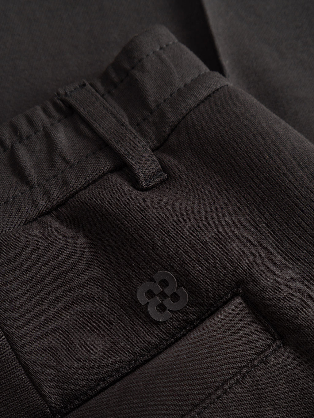 Close-up of the Gabba GABmonza Cropped Tasca Lock Pant in Meteorite, featuring mid-weight interlock fabric with detailed views of the waistband, belt loop, pocket, and a small embroidered logo above the pocket.