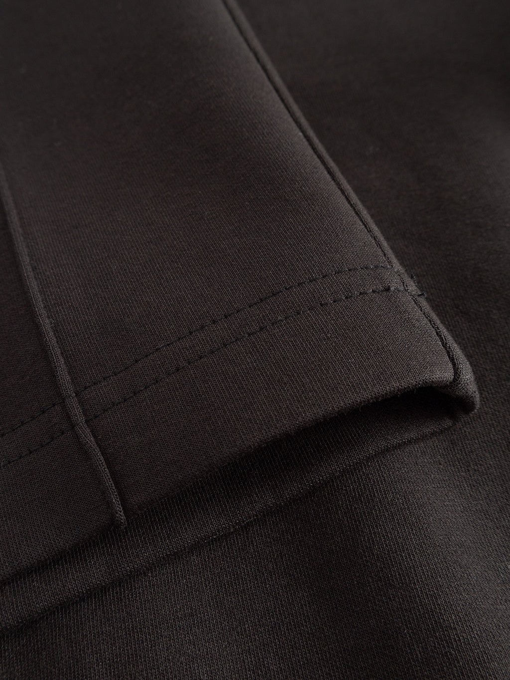Close-up of black mid-weight interlock fabric with visible stitching, showing the edge of a folded GABmonza Cropped Tasca Lock Pant by Gabba in Meteorite, set against a dark background.