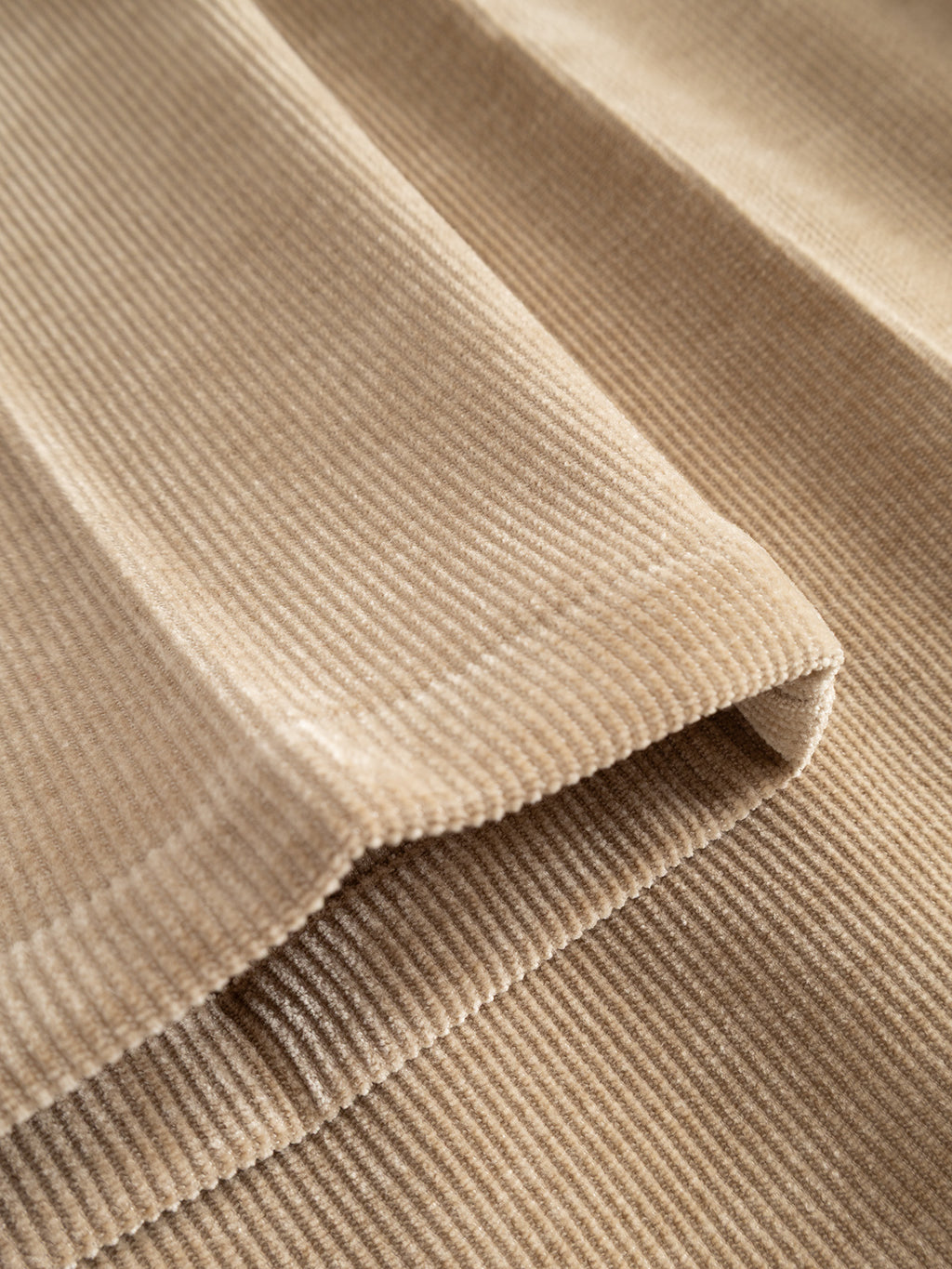Close-up of folded sand-colored Crocker corduroy fabric highlighting its soft, ribbed texture and parallel ridges—perfect for the Gabba GABmonza Cropped Tasca Fune Pant, a relaxed straight fit jersey corduroy pant with a cropped leg.