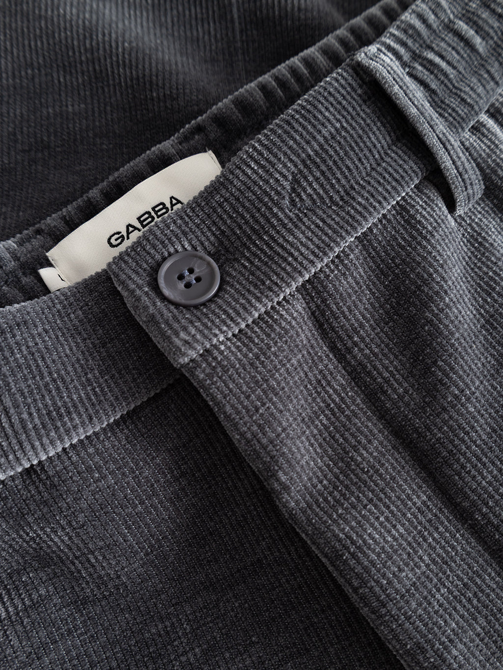 Close-up of GABmonza Cropped Tasca Fune Pants in Turbulence Blue by Gabba, made from jersey corduroy with a black button, relaxed straight fit, and a visible white GABBA label inside the elastic waistband.