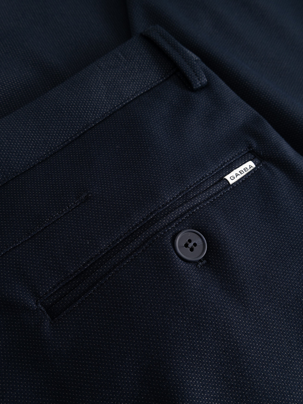Close-up of the Gabba GABpaul Dotty Pant in navy, highlighting a back welt pocket with button closure and a small white GABBA label above the pocket. Crafted from superstretch fabric with a subtle dotted micro-pattern weave, these pants offer both comfort and modern style.