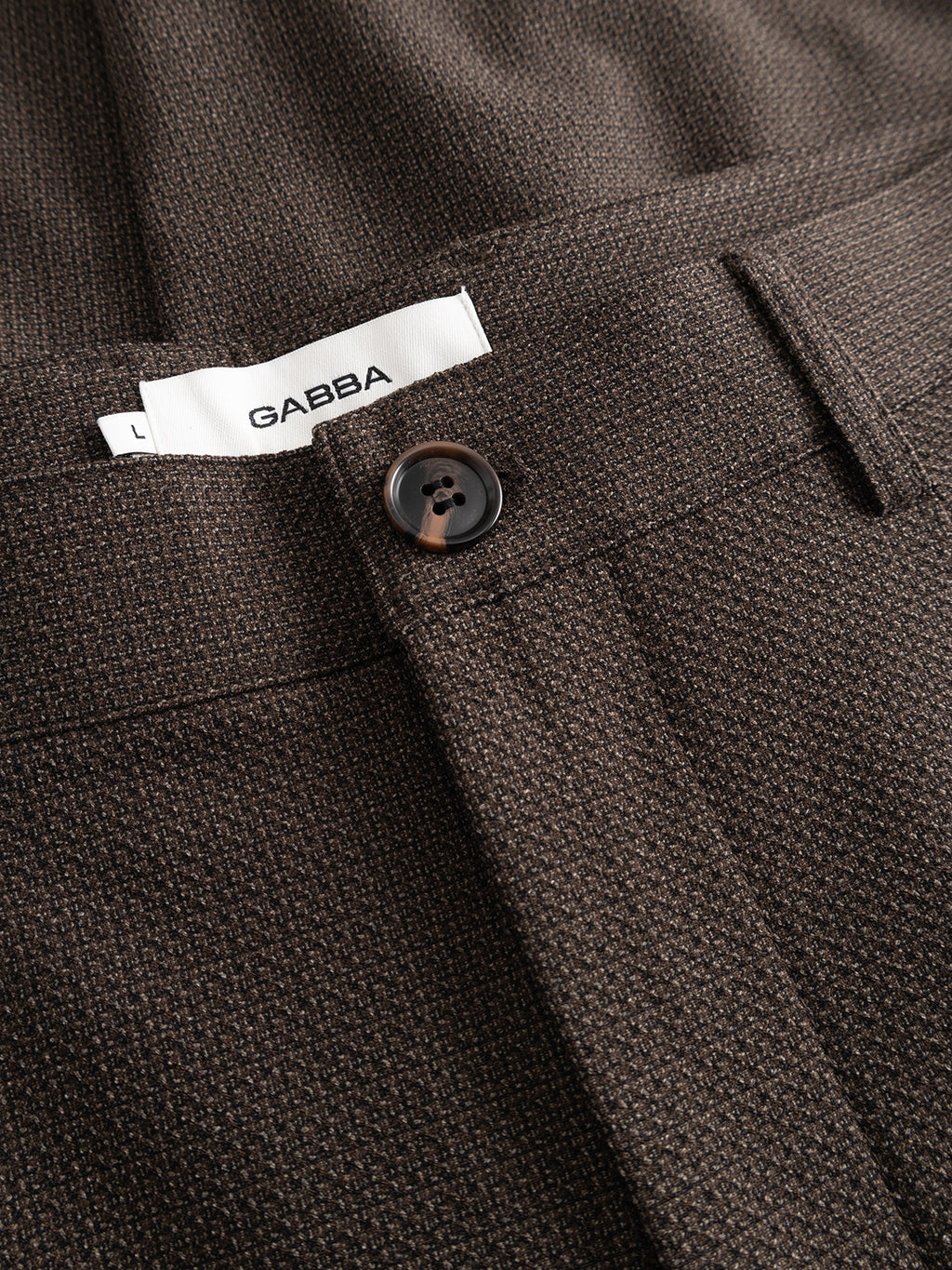 Close-up of brown textured dobby fabric GABjoe-pas Rubin Pant - Brown Slate by Gabba, featuring a dark button and a partially visible white “GABBA” L label inside the waistband.