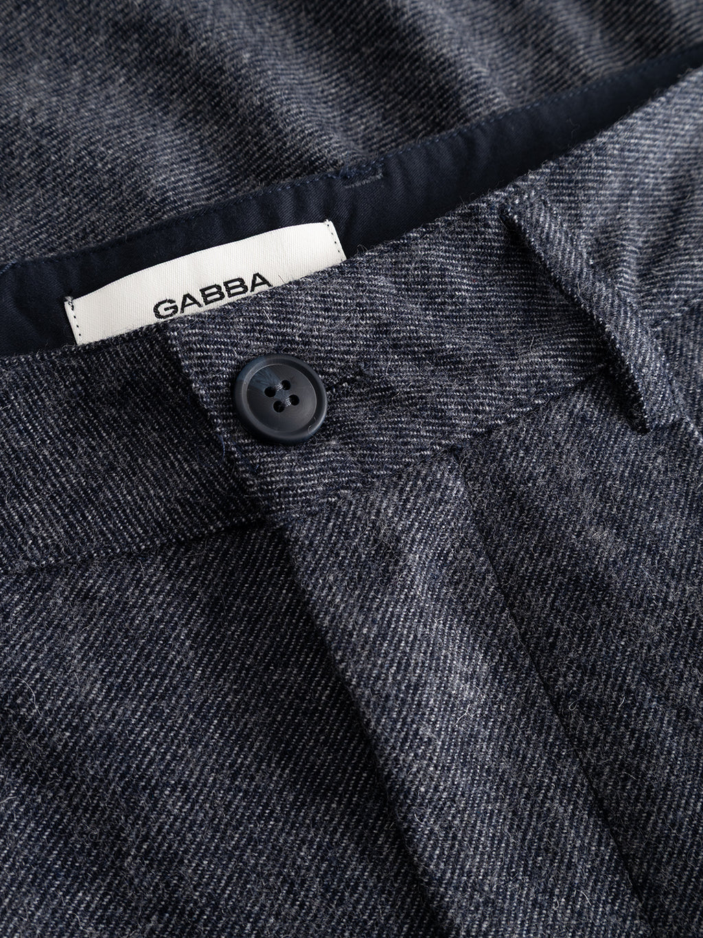Close-up of the GABdavid Twilight Pant in Navy by Gabba, featuring a button closure and a white Gabba label inside the waistband. The fabric has a subtle textured finish with a dark wash, offering a loose tapered fit that blends comfort with modern style.