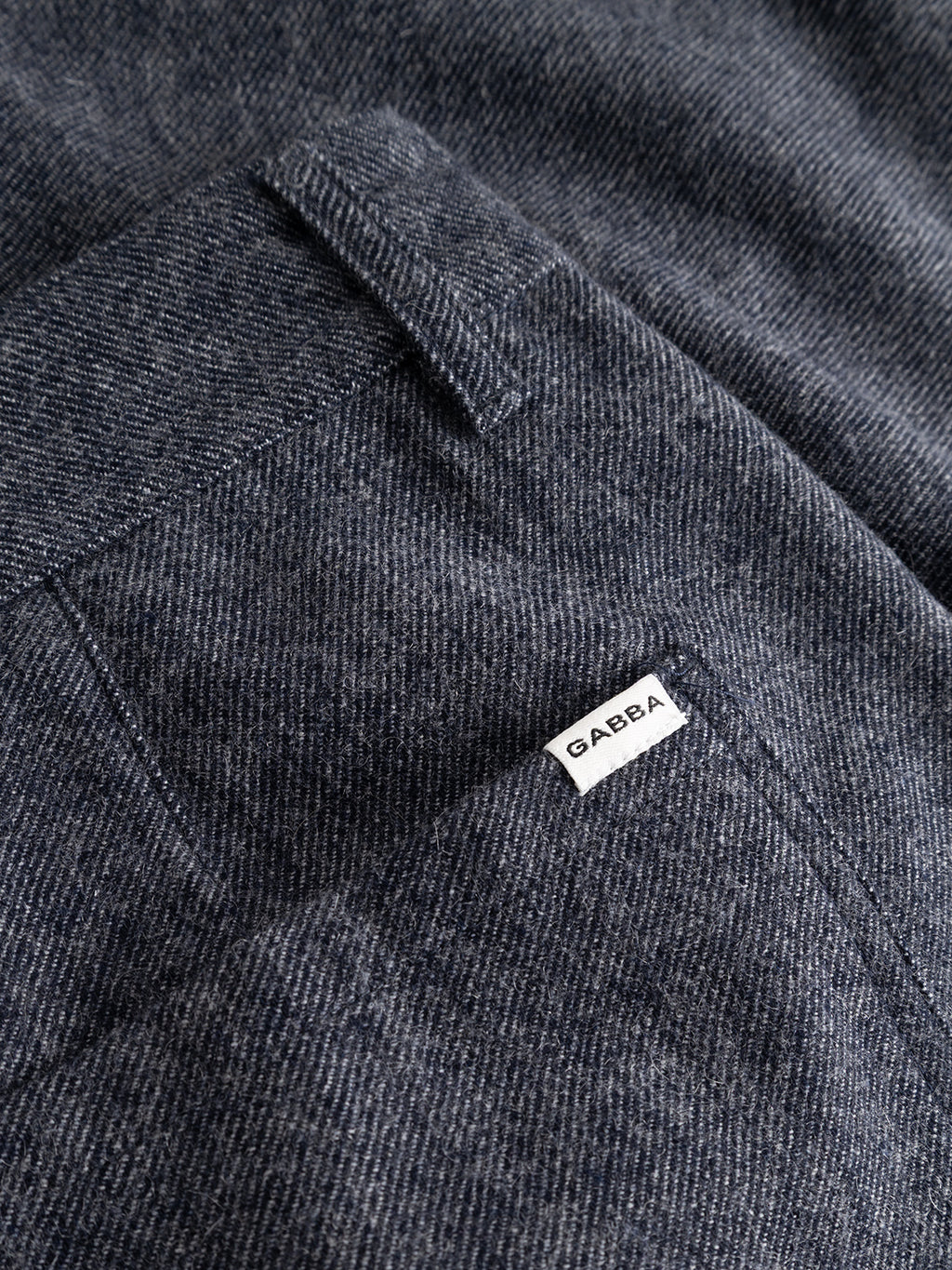 Close-up of navy fabric from the Gabba GABdavid Twilight Pant, featuring visible stitching, a pocket, and a small white label with “Gabba” text. The texture of the material is clearly detailed, showcasing the refined quality characteristic of contemporary chino designs.