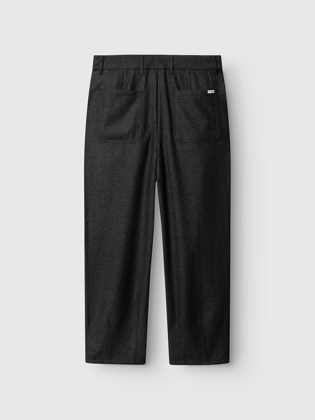The Gabba GABdavid Twilight Pant in dark grey is pictured from the back, highlighting two rear pockets and a small white tag above the right pocket, set against a plain light gray background. These contemporary wool-blend twill chinos offer a loose tapered fit for modern comfort and style.